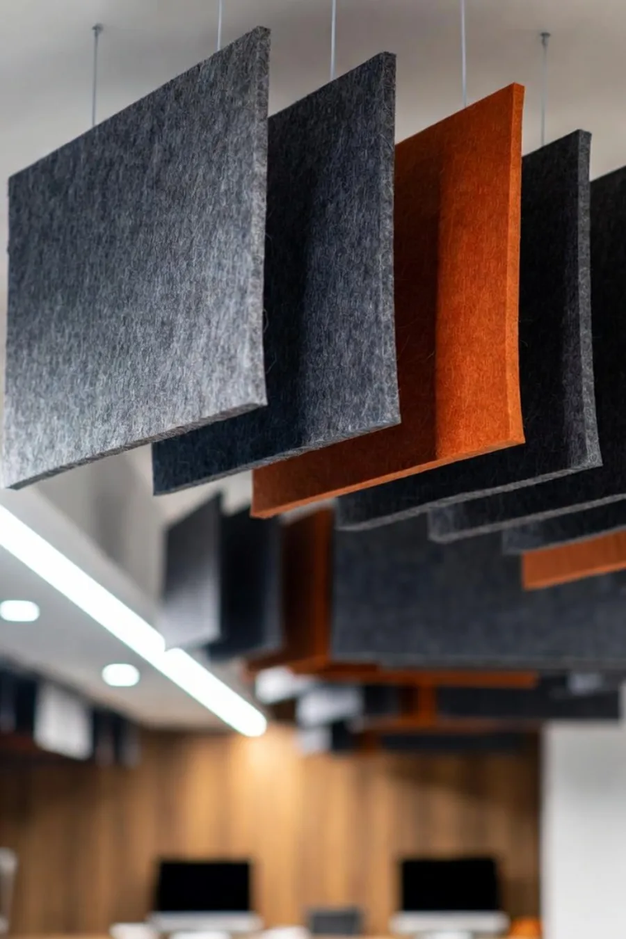 Baffles acoustiques en feutre charbon et terracotta suspendus au-dessus des postes de travail